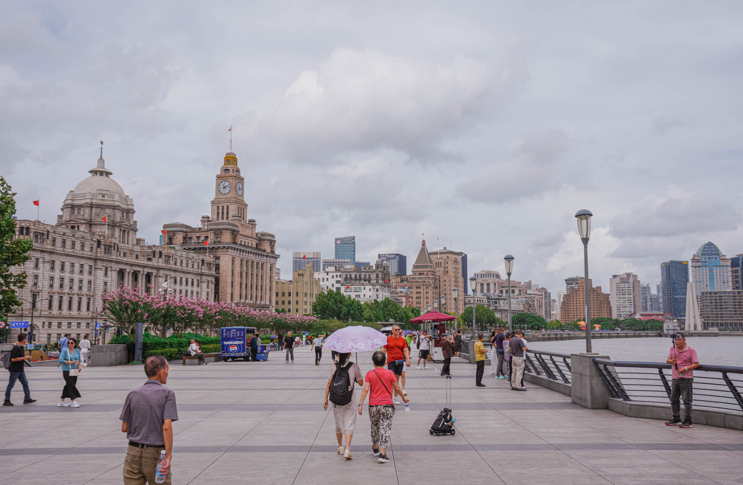 Strolling along the Bund waterfront in Shanghai with rows of historic colonial-era buildings on one side and the silhouettes of modern skyscrapers across the river, an open-air museum of Art Deco and neoclassical architecture where East meets West.