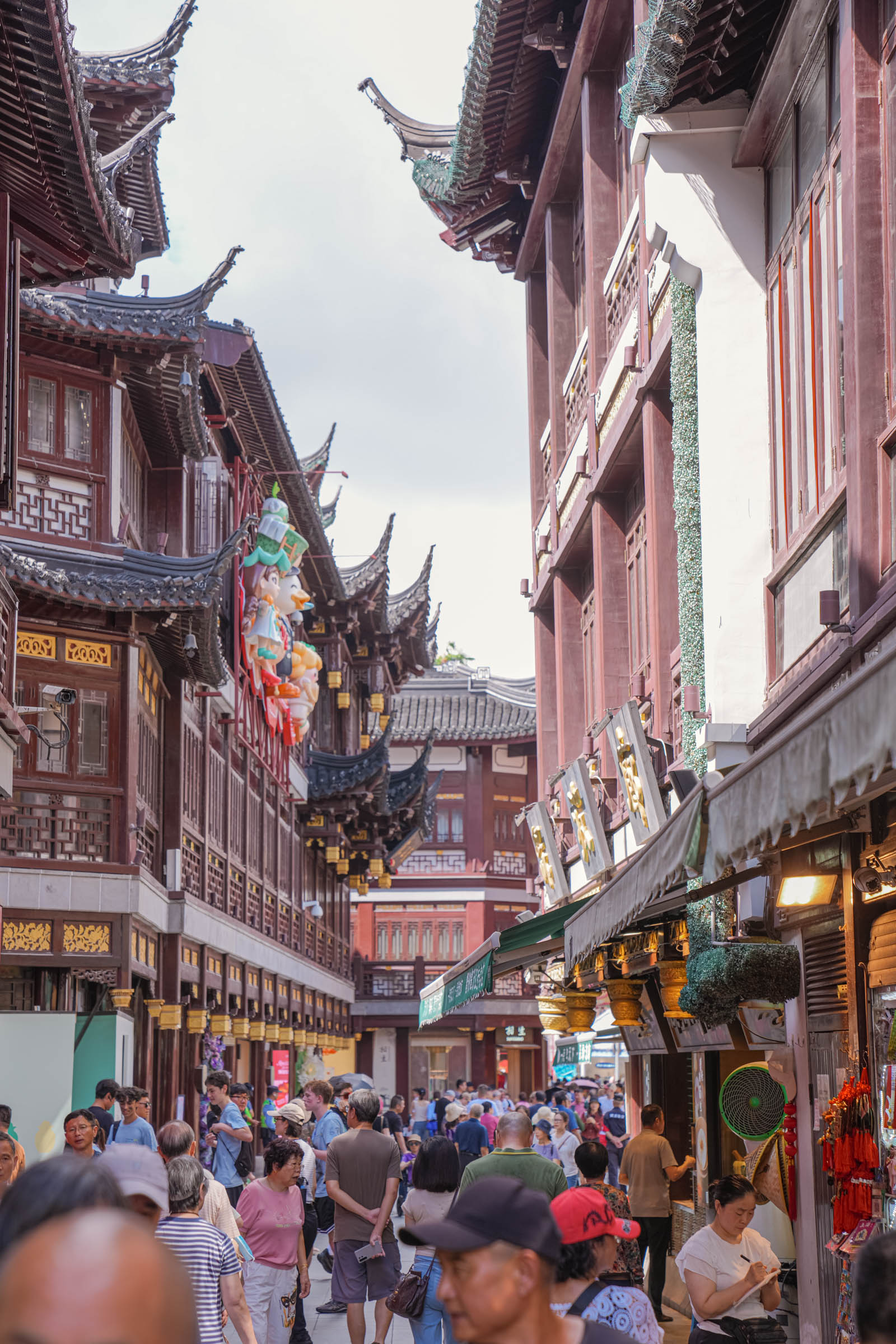 The famous zigzag Nine-Bend Bridge leading to the Mid-Lake Huxinting Teahouse in the Yu Garden Bazaar – an ancient stone bridge winding over a pond with tourists crossing toward a traditional wooden tea house.