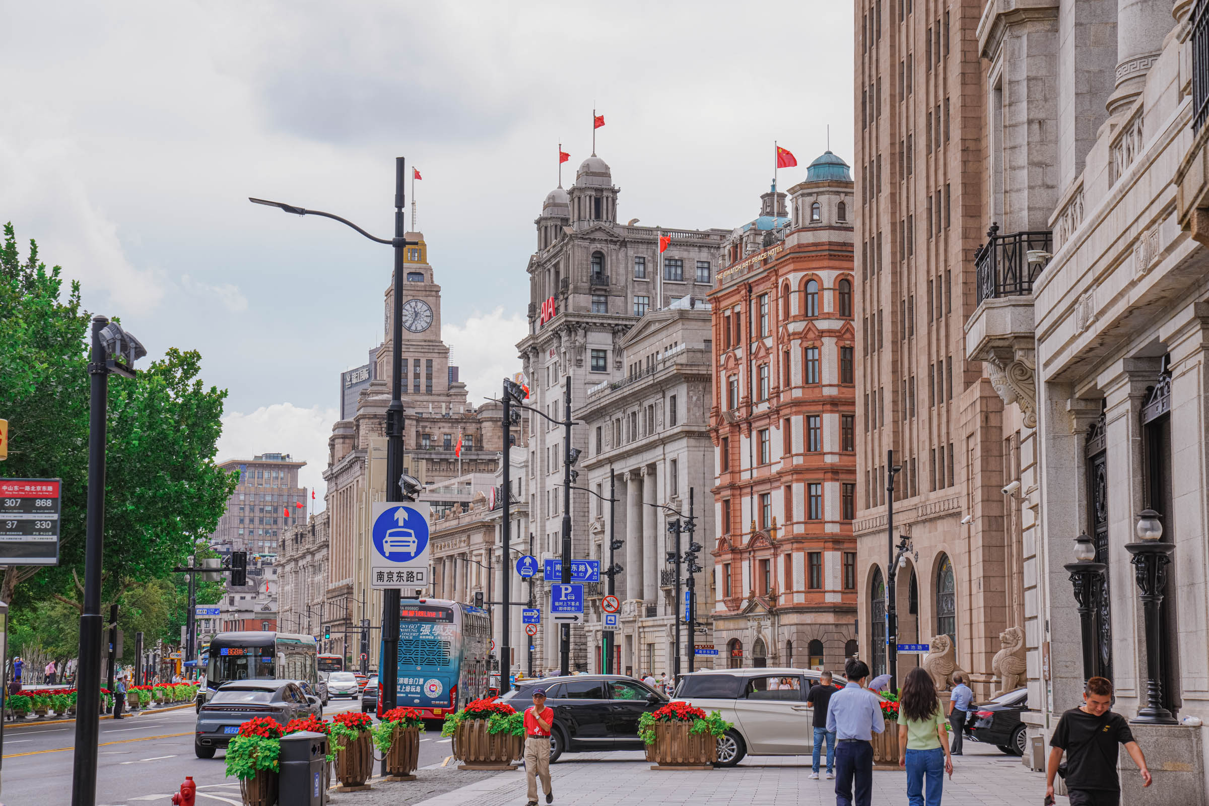 Urban street in central Shanghai lined with early 20th-century European-style buildings and tree-lined sidewalks, busy with city traffic and pedestrians, showcasing the city’s cosmopolitan architectural heritage.