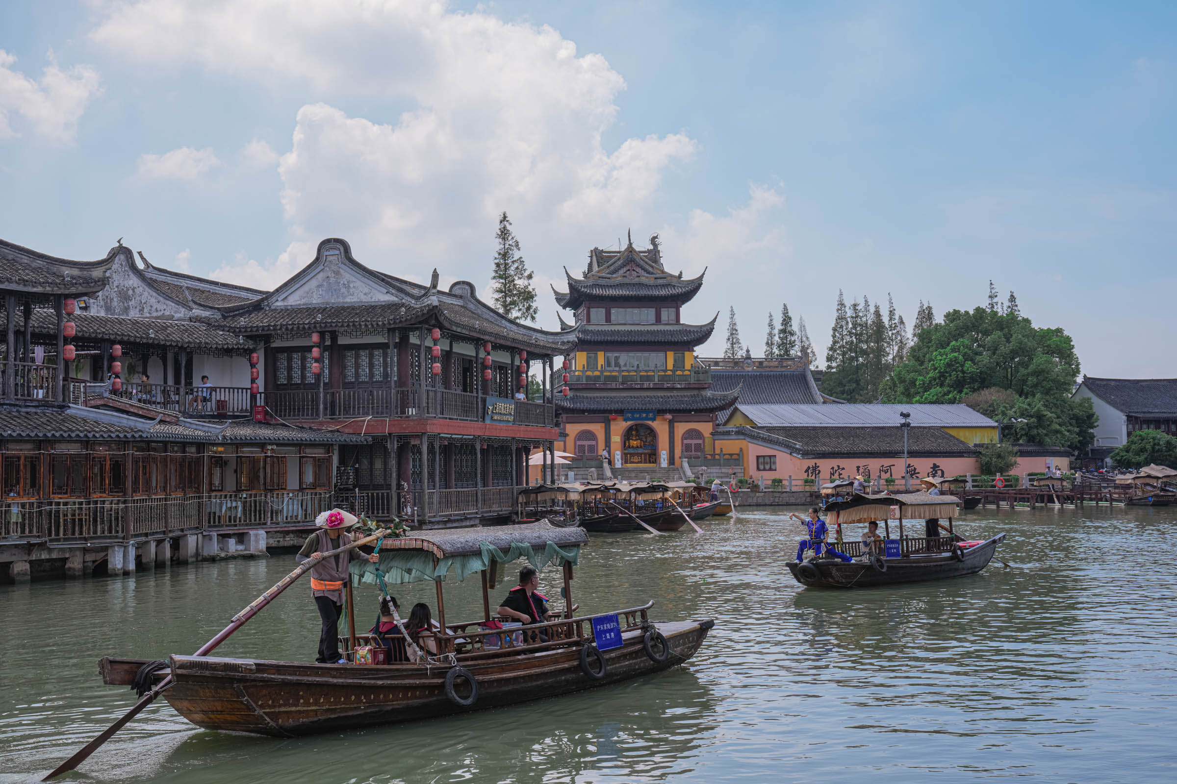 A local boatman paddling a wooden sampan under a small stone bridge in Zhujiajiao’s canal network, passing by riverside buildings as he offers a glimpse into the slow-paced, traditional lifestyle preserved just outside modern Shanghai.