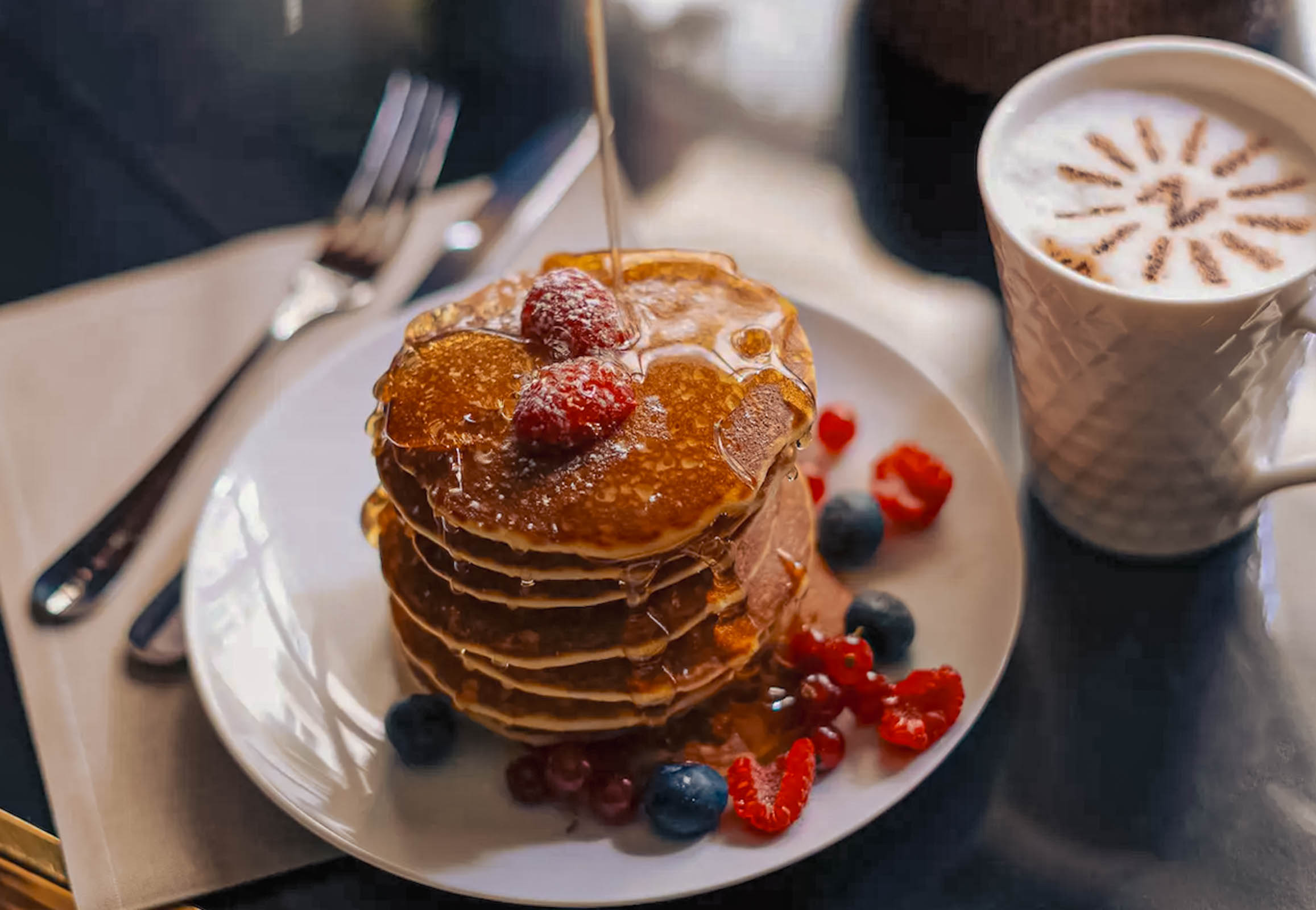 Breakfast at Hôtel Napoléon Paris: a stack of pancakes with fresh berries beside a cappuccino bearing the hotel's "N" monogram