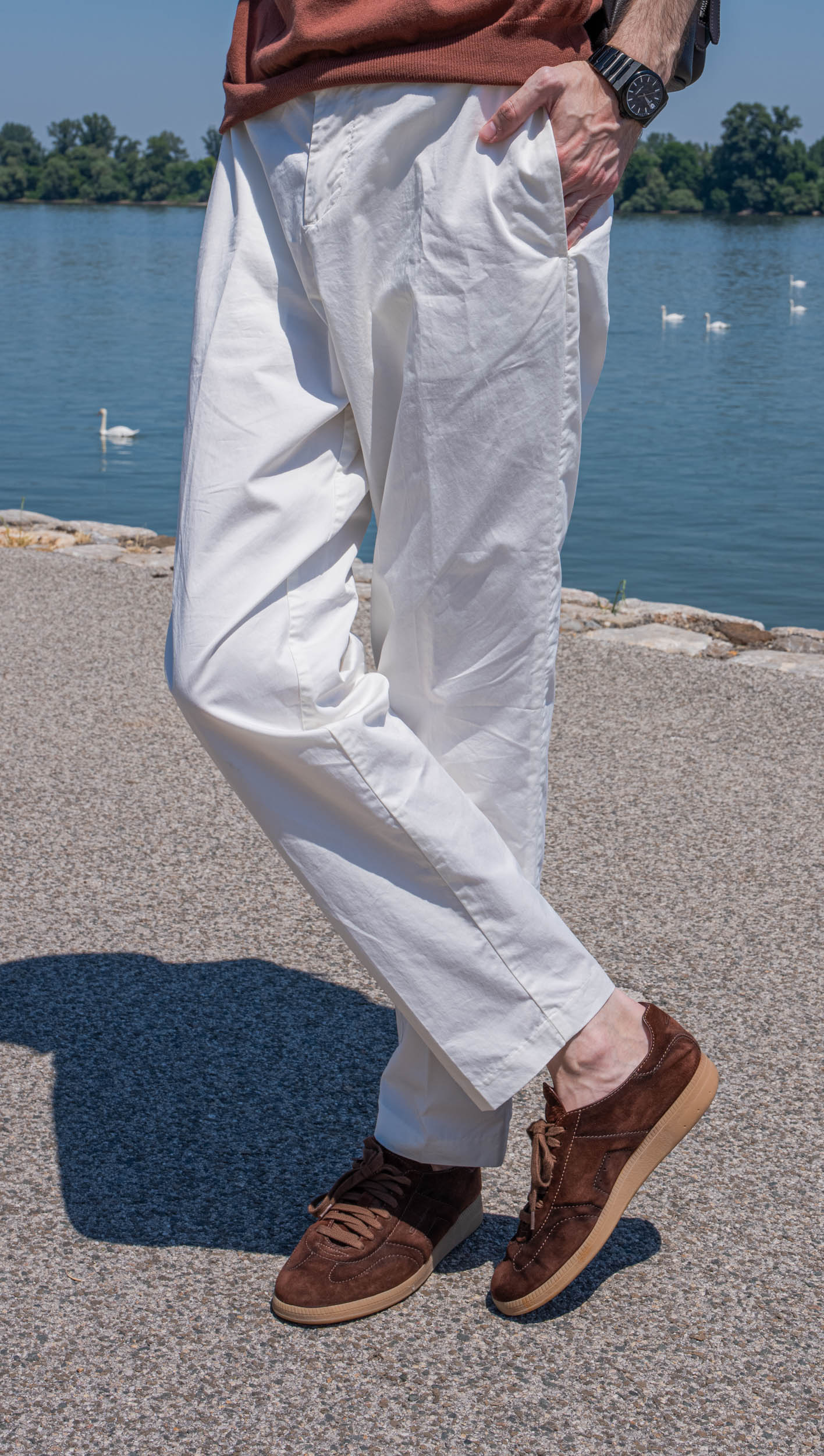 Close crop of Marko Tadić's white Kiton cotton trousers with one hand tucked into the pocket and the Biatec Fusion 03 watch showing at the wrist, swans and the Danube shoreline softly blurred behind.