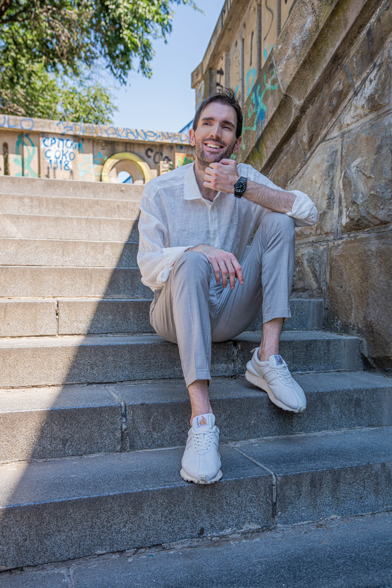 Marko Tadić, founder of the Mr.M blog, sitting on Belgrade stairs in a summer outfit with the Biatec Fusion 03 watch resting on his knee