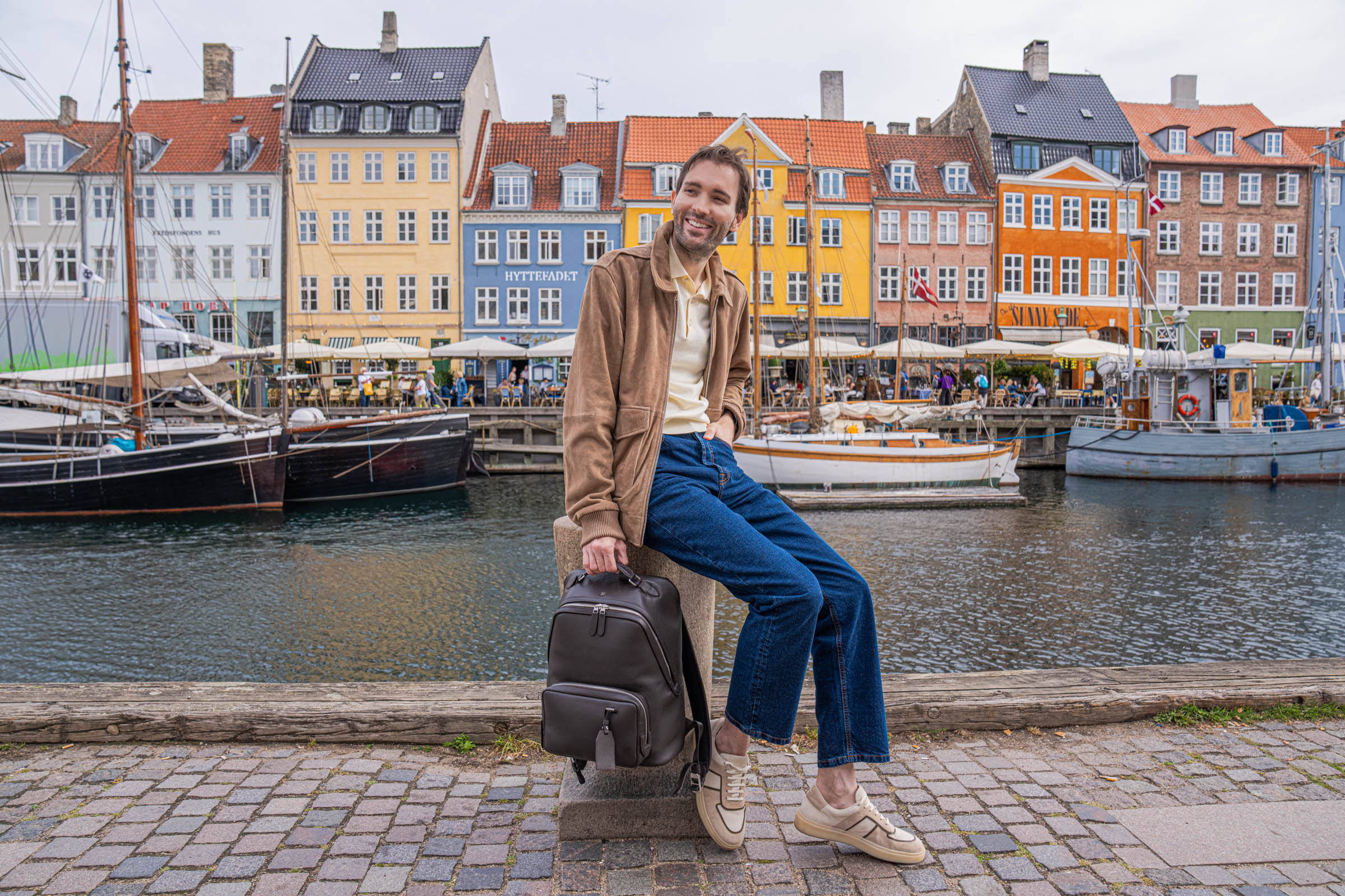 Marko Tadić, founder of Mr.M blog, in a suede jacket and jeans with a leather backpack on the Nyhavn quay