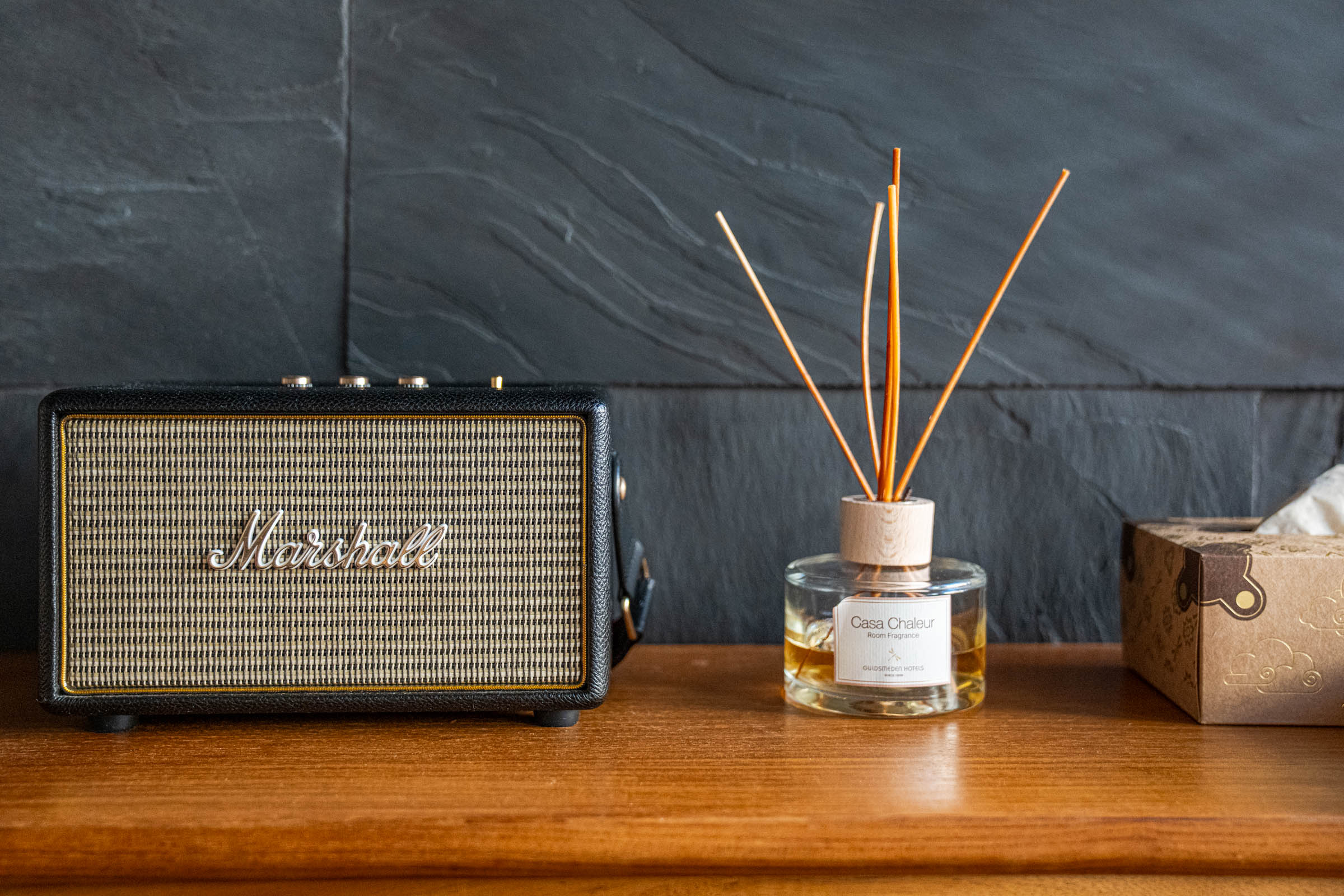Marshall speaker and Casa Chaleur reed diffuser on a teak console against a black slate wall, photo by Marko Tadić, founder of Mr.M blog