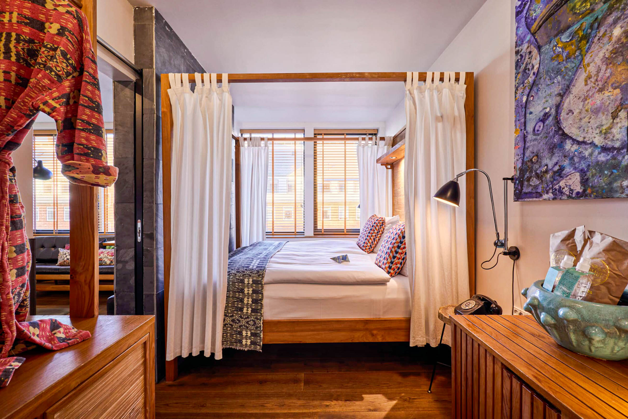 Teak four-poster bed with white linen curtains, indigo throw and slate wall in the Classic Suite at Manon Les Suites Guldsmeden Copenhagen