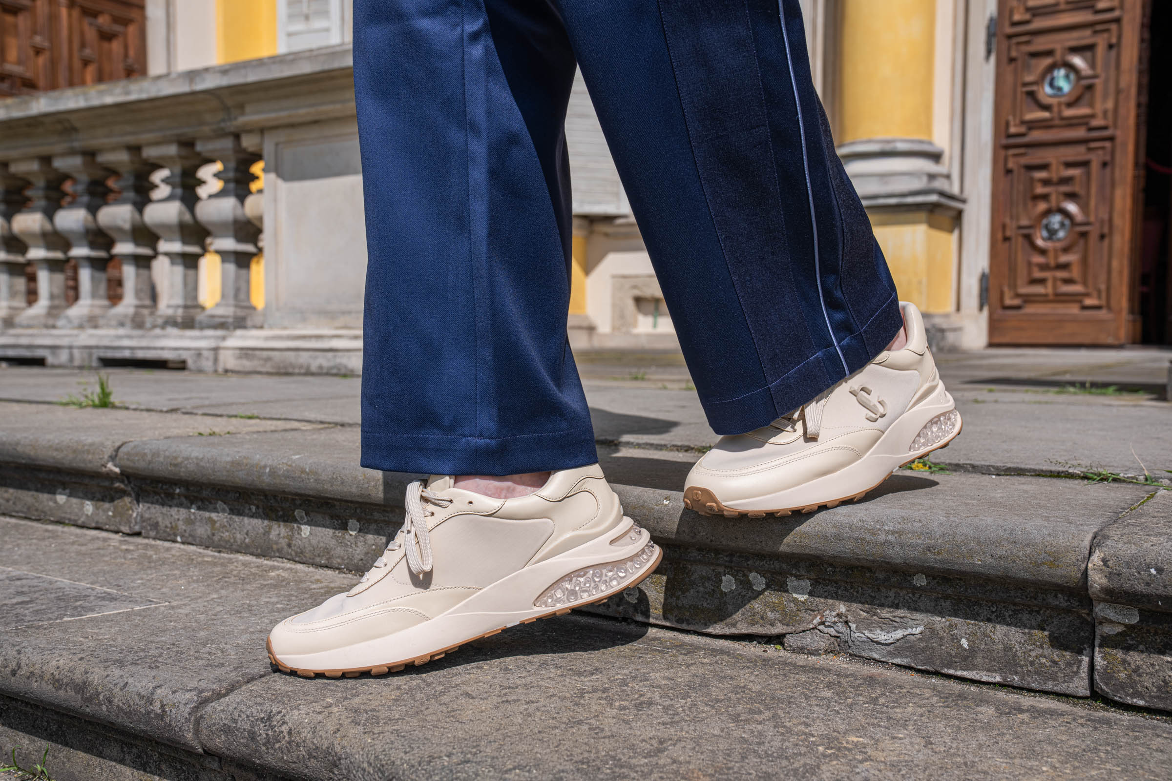 Close-up of the natural leather Jimmy Choo Memphis sneakers and the clean turned hem of the navy BLUEMARBLE trousers.