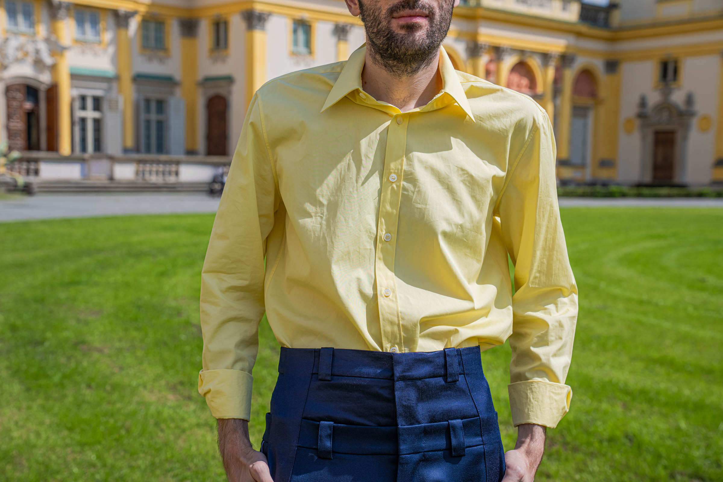 Close-up of the yellow Ferragamo cotton shirt tucked into the doubled waistband of navy BLUEMARBLE Paris trousers.