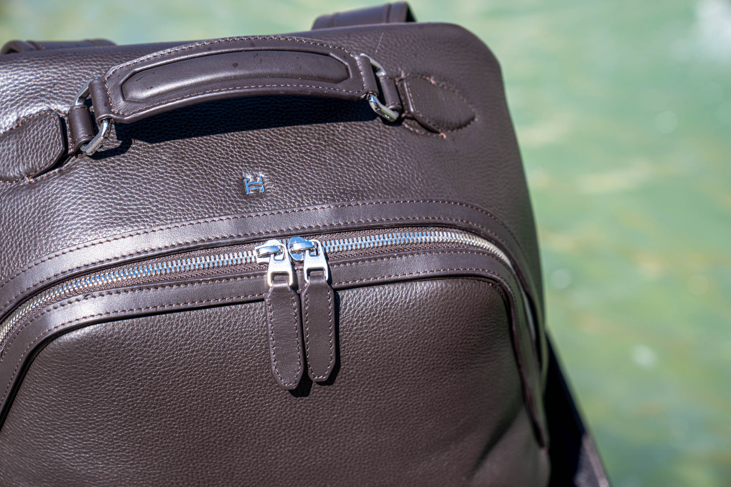 Top view of the dark brown 1900 leather backpack with its architectural diagonal zip line and padded carry handle, photographed beside a Copenhagen fountain
