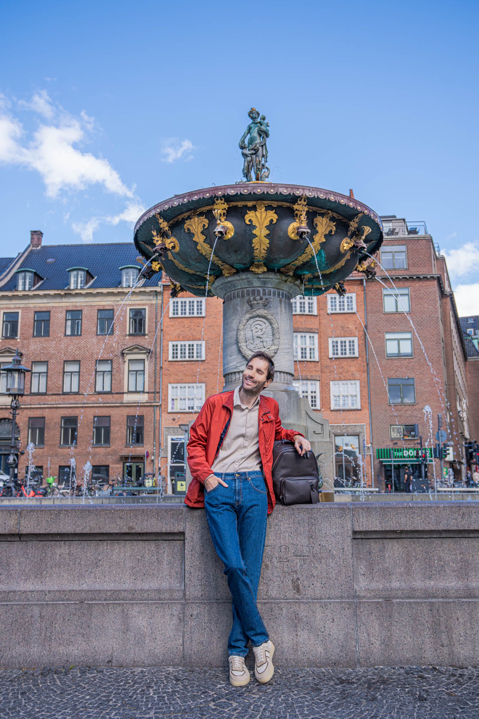 Fashion blogger Marko Tadić in a red Canali field jacket and beige Giannetto Portofino flannel shirt, holding a dark brown 1900 Tempo Grande leather backpack in Copenhagen