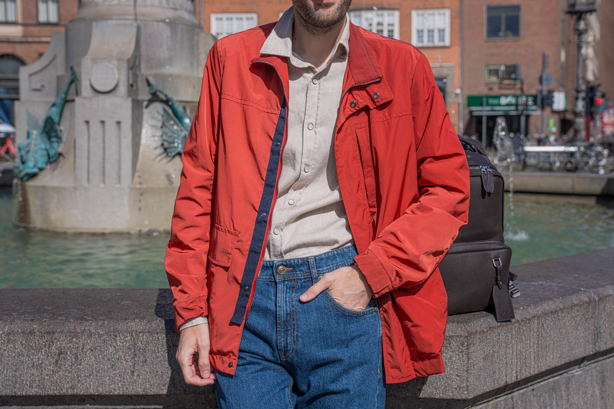 Close up of the red Canali field jacket worn open over a sand beige cotton flannel shirt and Versace jeans, with a navy zip tape and snap placket detail visible