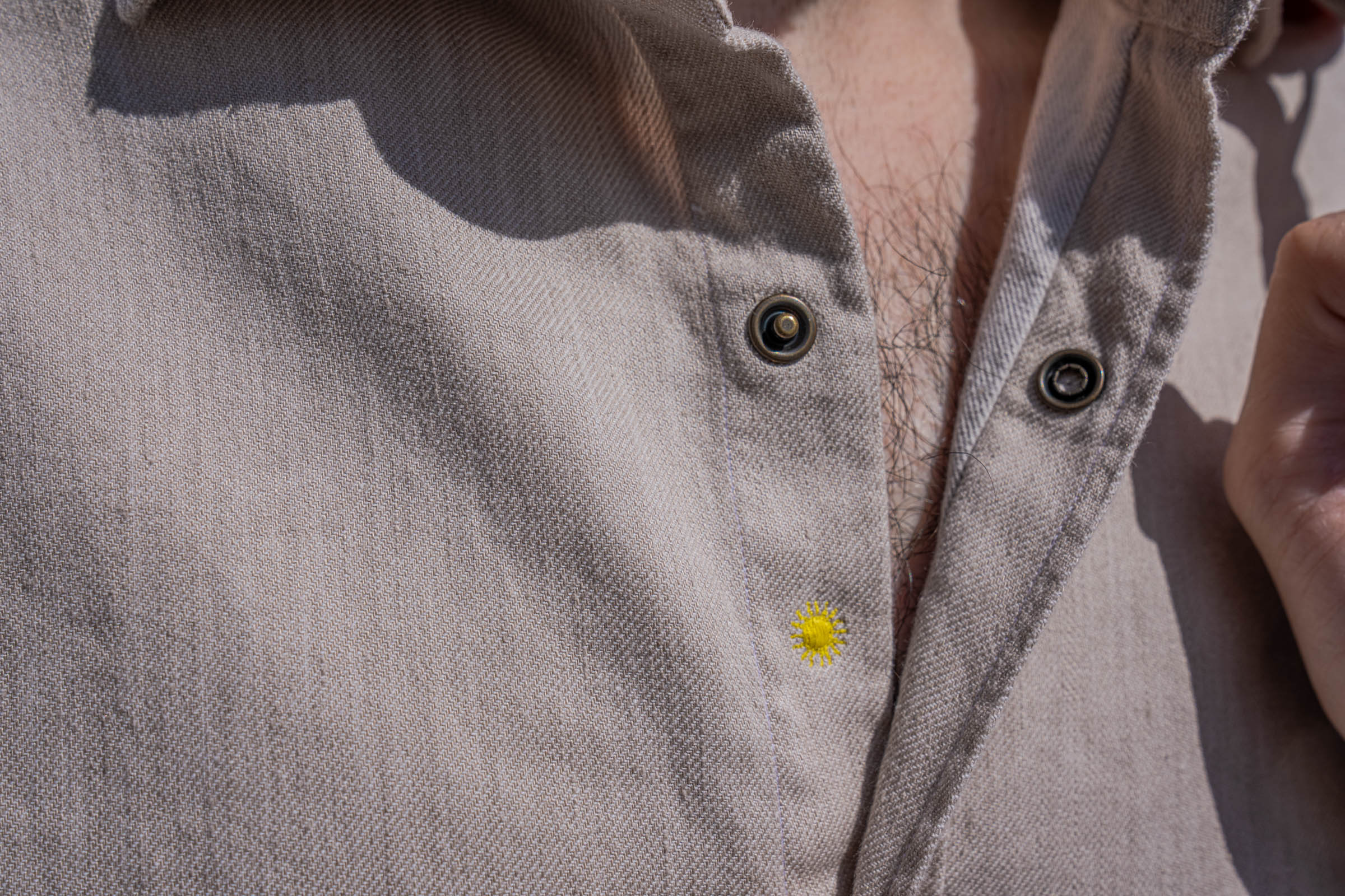 Macro detail of the small yellow embroidered sun and pearl toned snap buttons on the beige Giannetto Portofino washed flannel shirt made in Italy