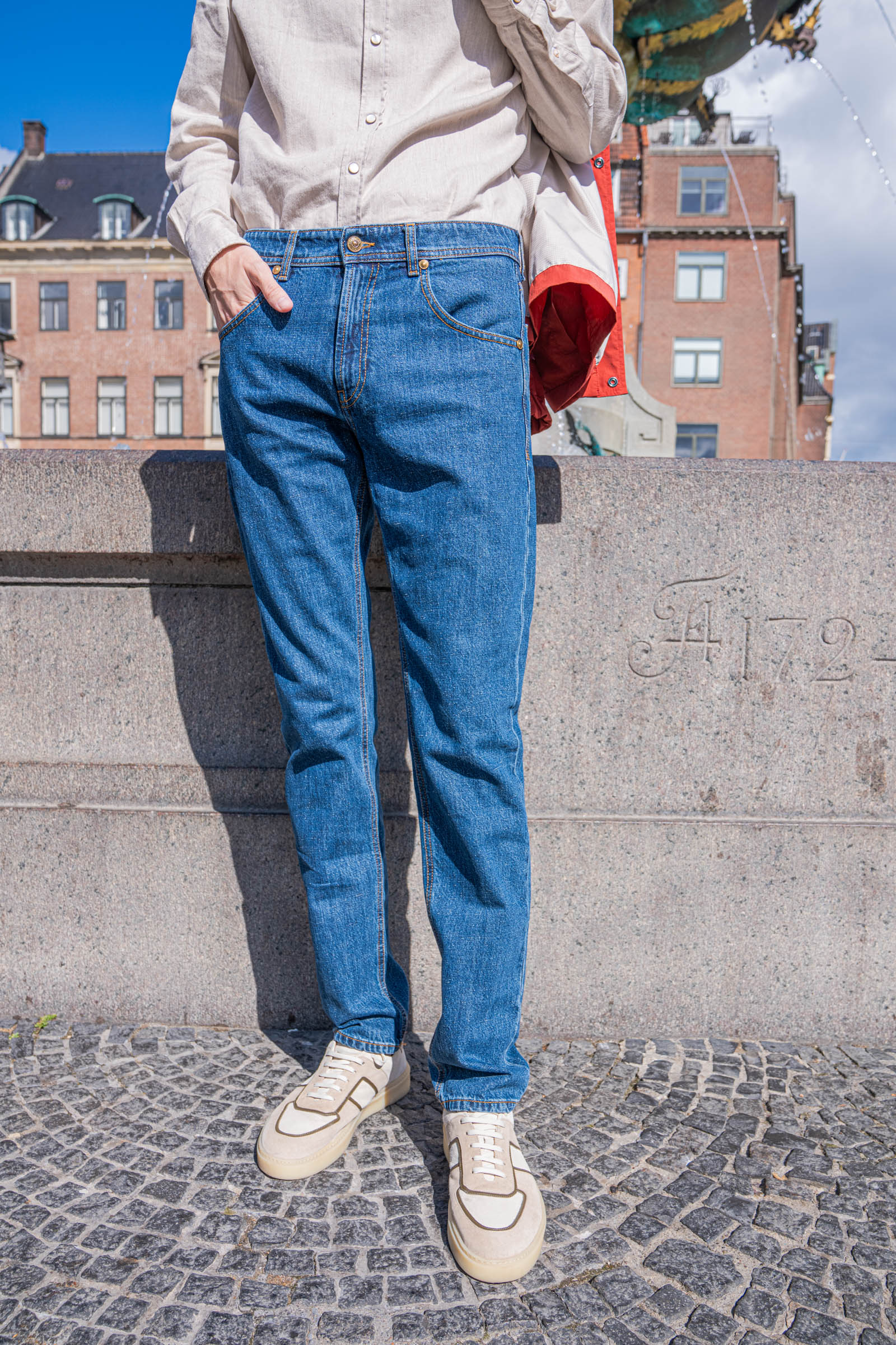 Men's denim styling detail showing the fit and break of Versace straight leg jeans over Carlos Santos suede sneakers on Gammeltorv square in Copenhagen