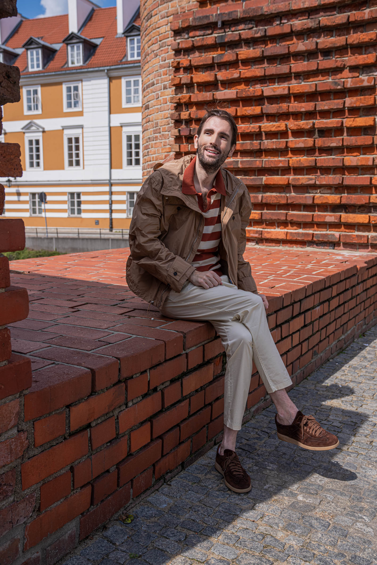 Marko Tadić sitting on the brick wall of the Warsaw Barbican in a summer menswear outfit