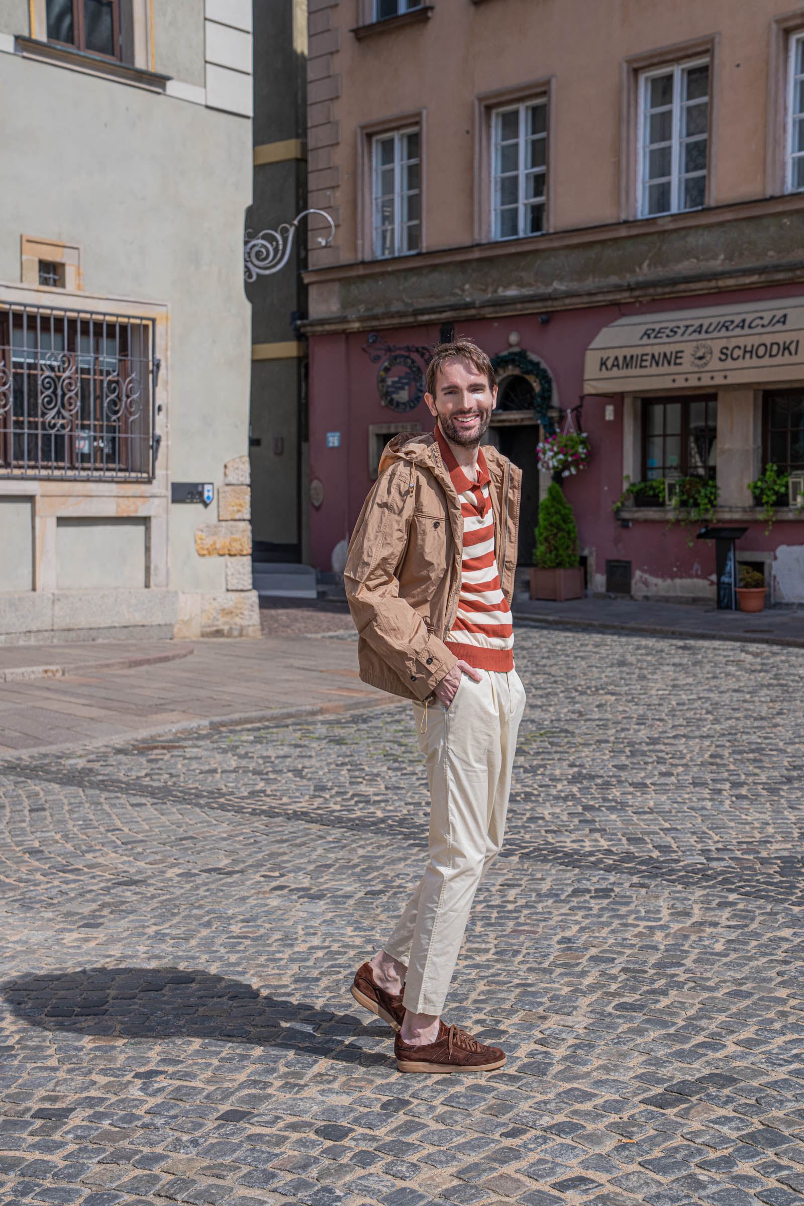 Marko Tadić walking across Warsaw's Old Town Market Square in a camel Ferragamo hooded jacket and cream trousers