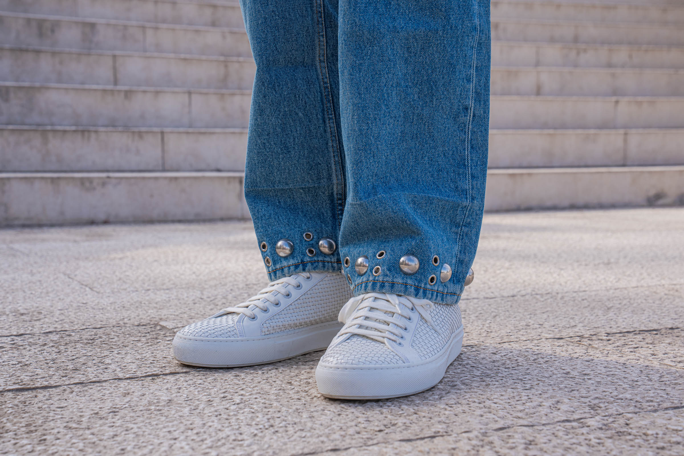 Valentino woven leather sneakers mid-step below the studded denim hem, on Marko Tadić