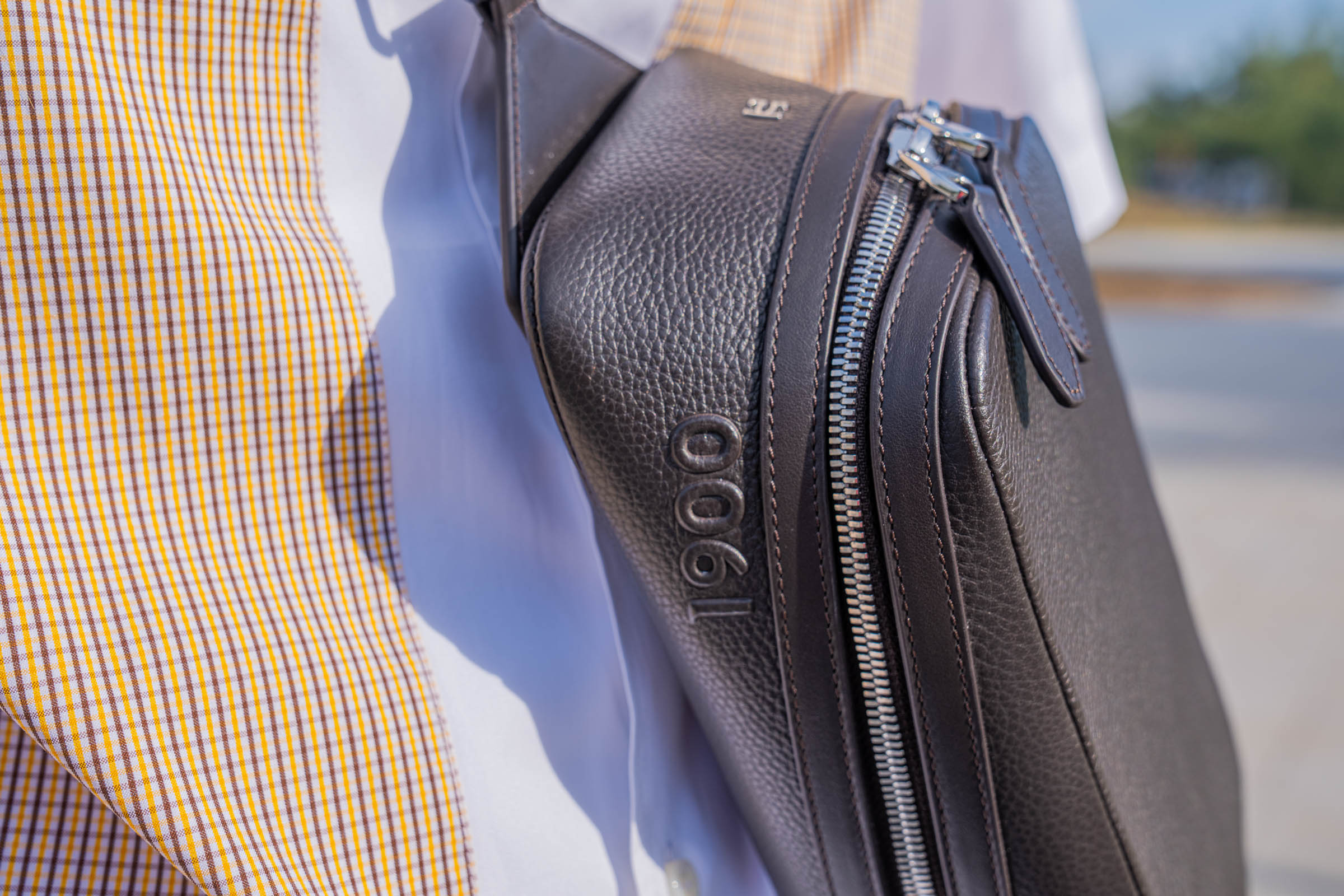 Detail of the 1900 Tempo Grande Crossbody bag worn by Marko Tadić, showing embossed 1900 lettering, angled silver zip and metal emblem against a Dsquared2 check shirt