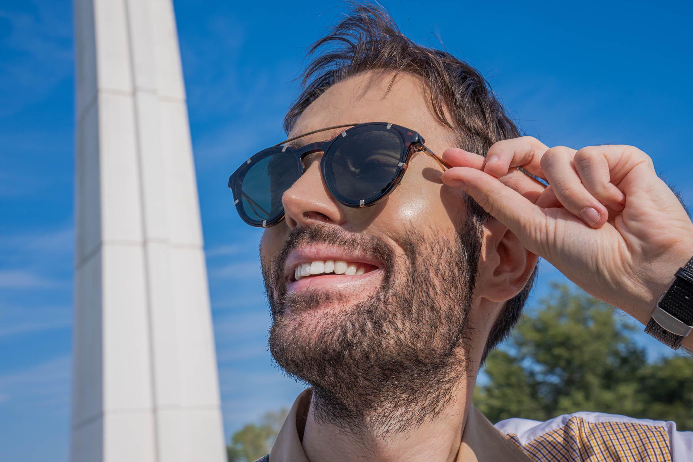 Smiling close-up portrait of Marko Tadić, founder of Mr.M by Marko Tadić, adjusting Givenchy round sunglasses with a gold-finish bridge and metal rim accents