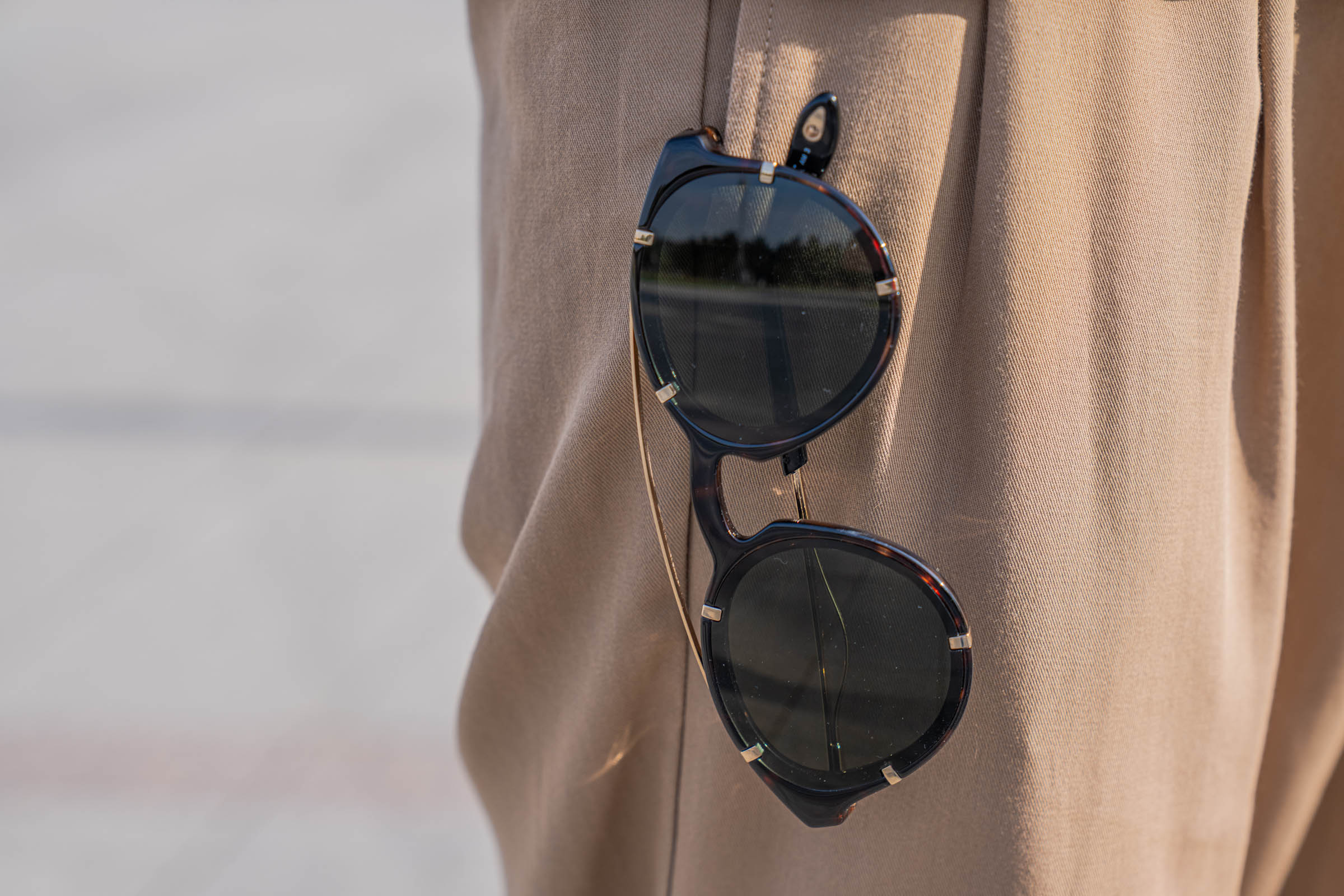 Close-up of Givenchy round sunglasses with metal rim studs hanging from the waistband of Marko Tadić, a quiet finishing touch to his Dsquared2 outfit