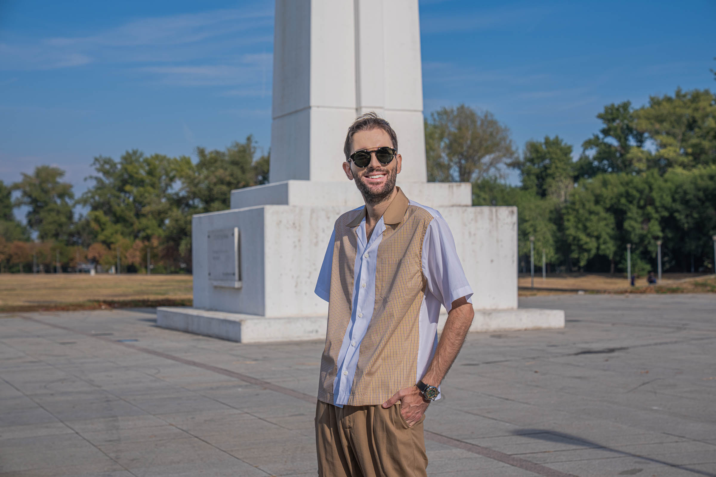 Horizontal portrait of Marko Tadić, founder of Mr.M by Marko Tadić, wearing a Dsquared2 outfit with camel collar shirt, Givenchy sunglasses and the Bard's Whisper Divine Comedy watch