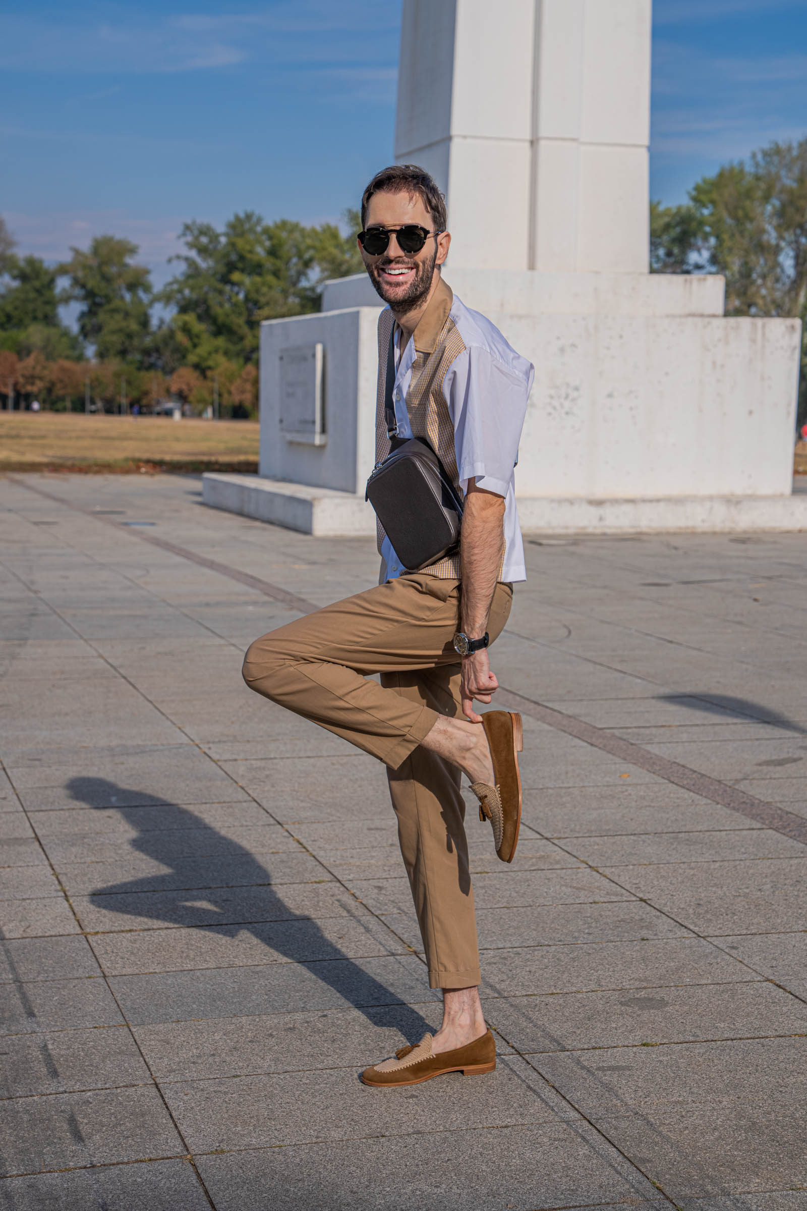 Playful pose by Marko Tadić, lifting one foot to show a Fratelli Rossetti Brera loafer with beige crochet vamp, styled with a Dsquared2 outfit and a 1900 bag