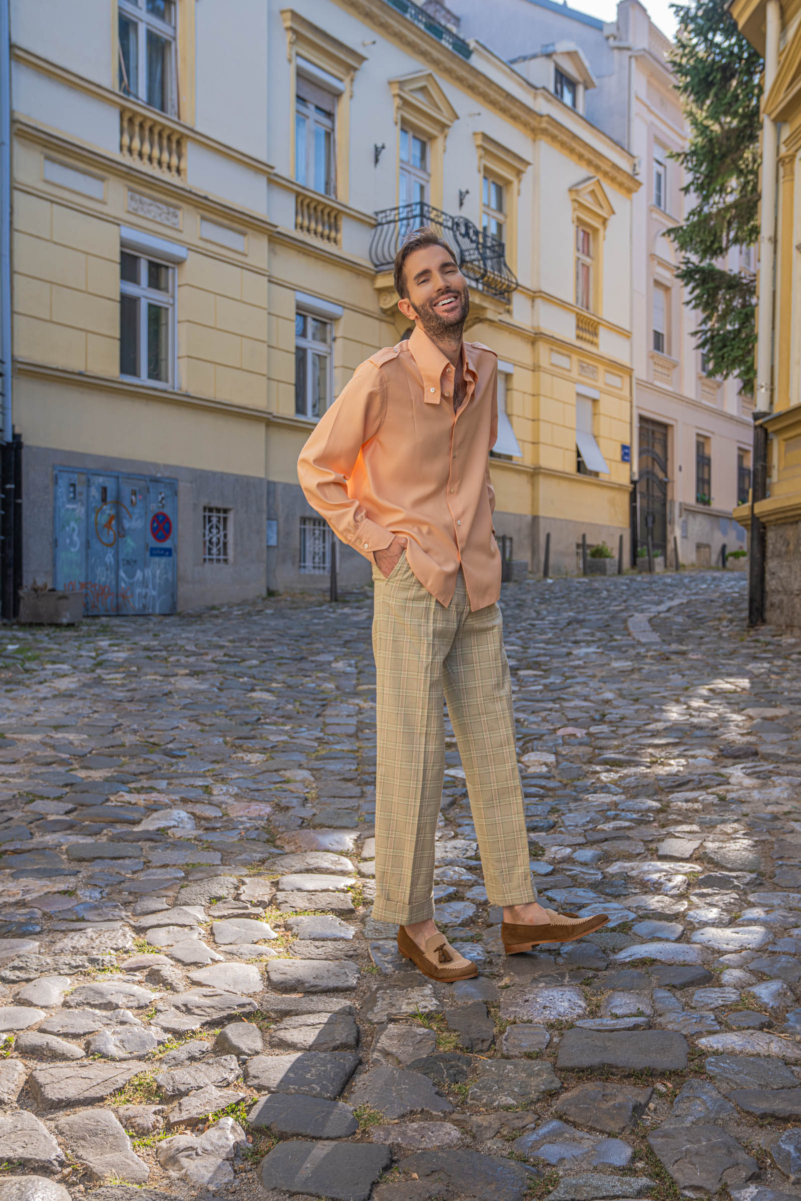 Marko Tadić of Mr.M laughs while touching his shirt collar, wearing Gucci check trousers and Brera tassel loafers