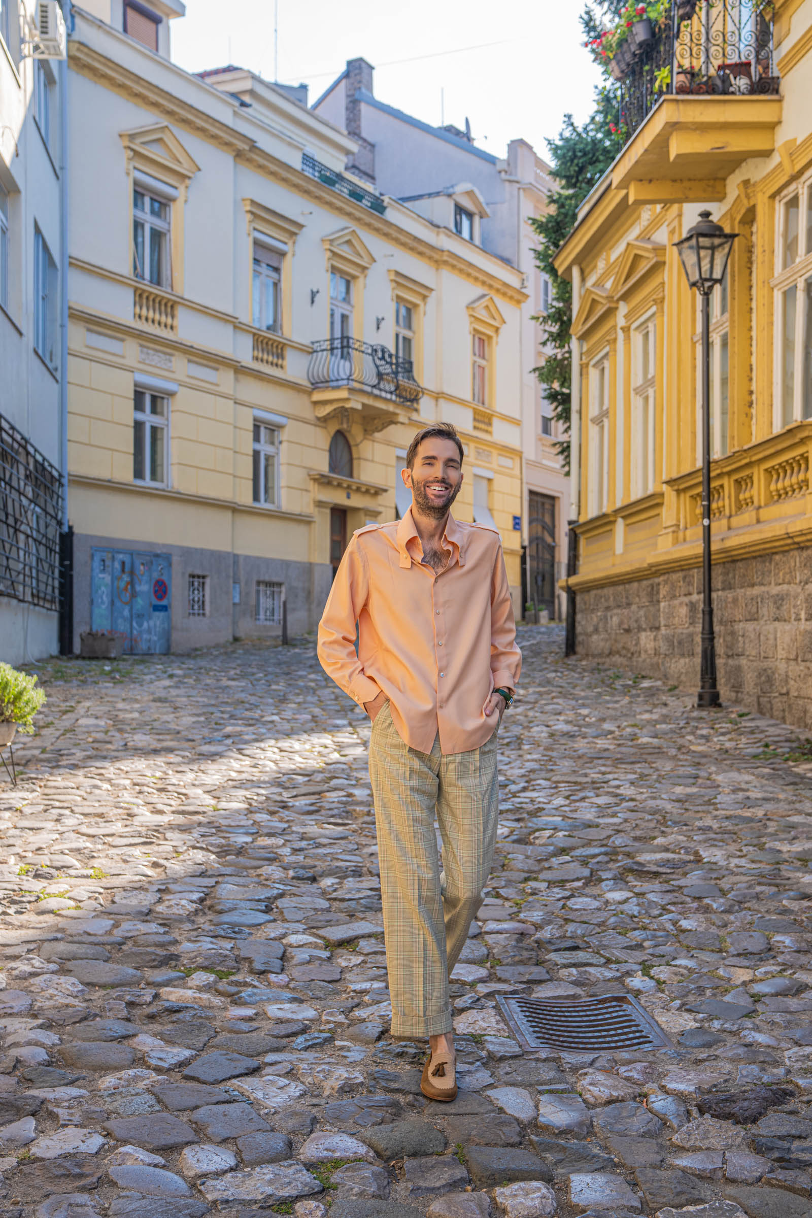 Fashion blogger Marko Tadić walks toward the camera in a peach Gucci silk shirt and wide Gucci check trousers