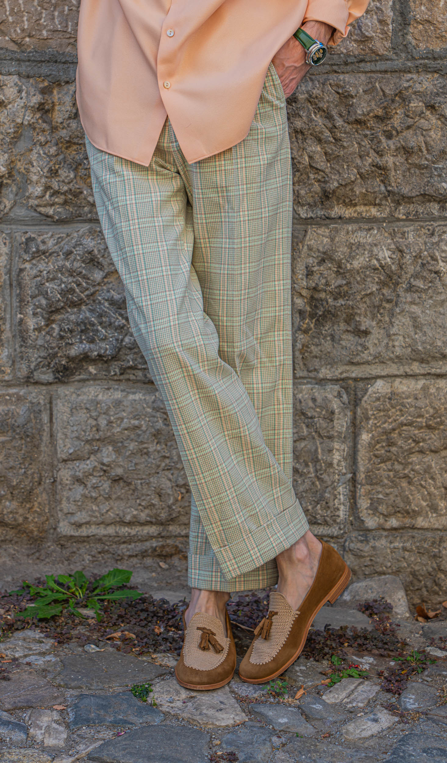 Marko Tadić leans on a stone wall, legs crossed, in Heritage Light Green check trousers and Brera crochet loafers