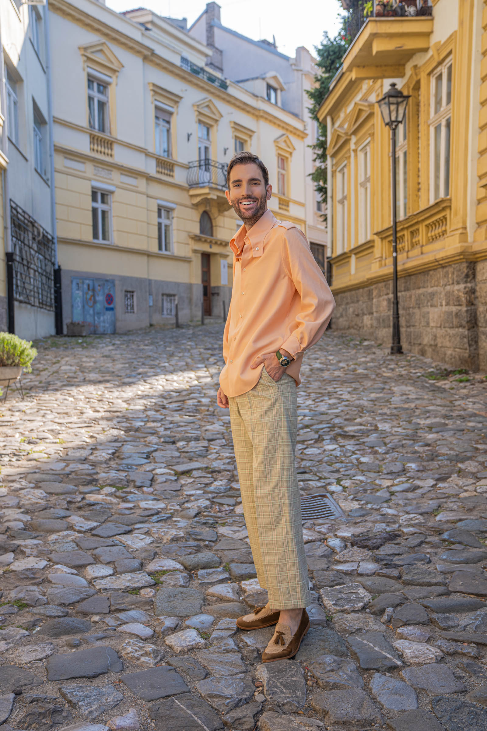 Three-quarter view of Marko Tadić in a peach Gucci shirt, glen check trousers and tobacco suede Brera loafers