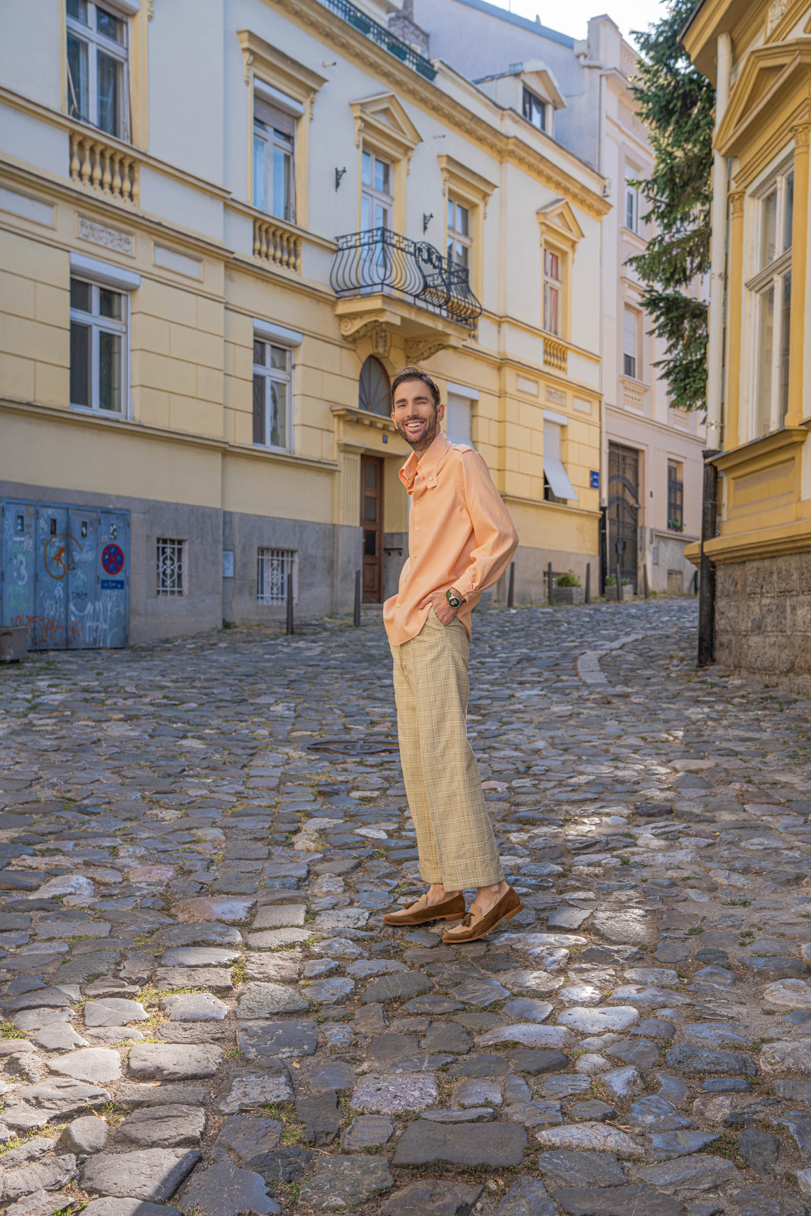 Full-length outfit by Marko Tadić: peach Gucci silk shirt, light green check trousers and Brera loafers on cobblestones