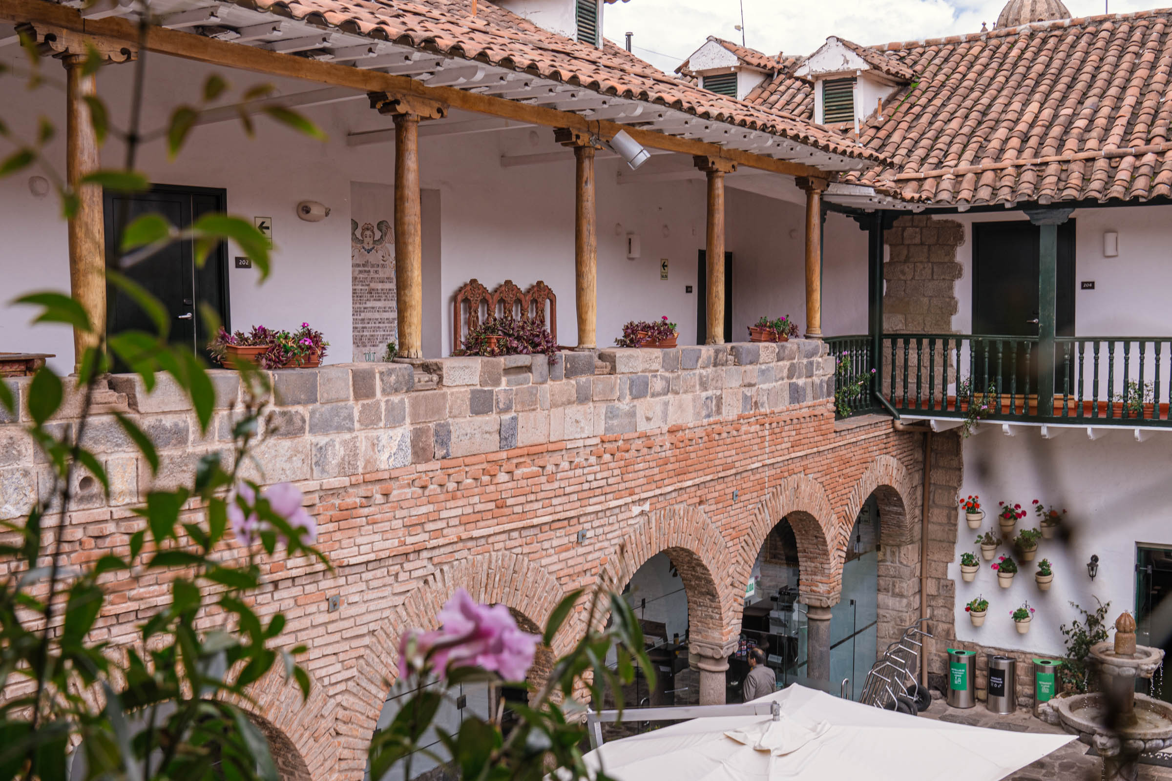 Gornja galerija unutrašnjeg dvorišta Casa Andina Premium Cusco hotela, sa drvenim gredama, zelenim balkonskim ogradama i cvećem u saksijama ispod.