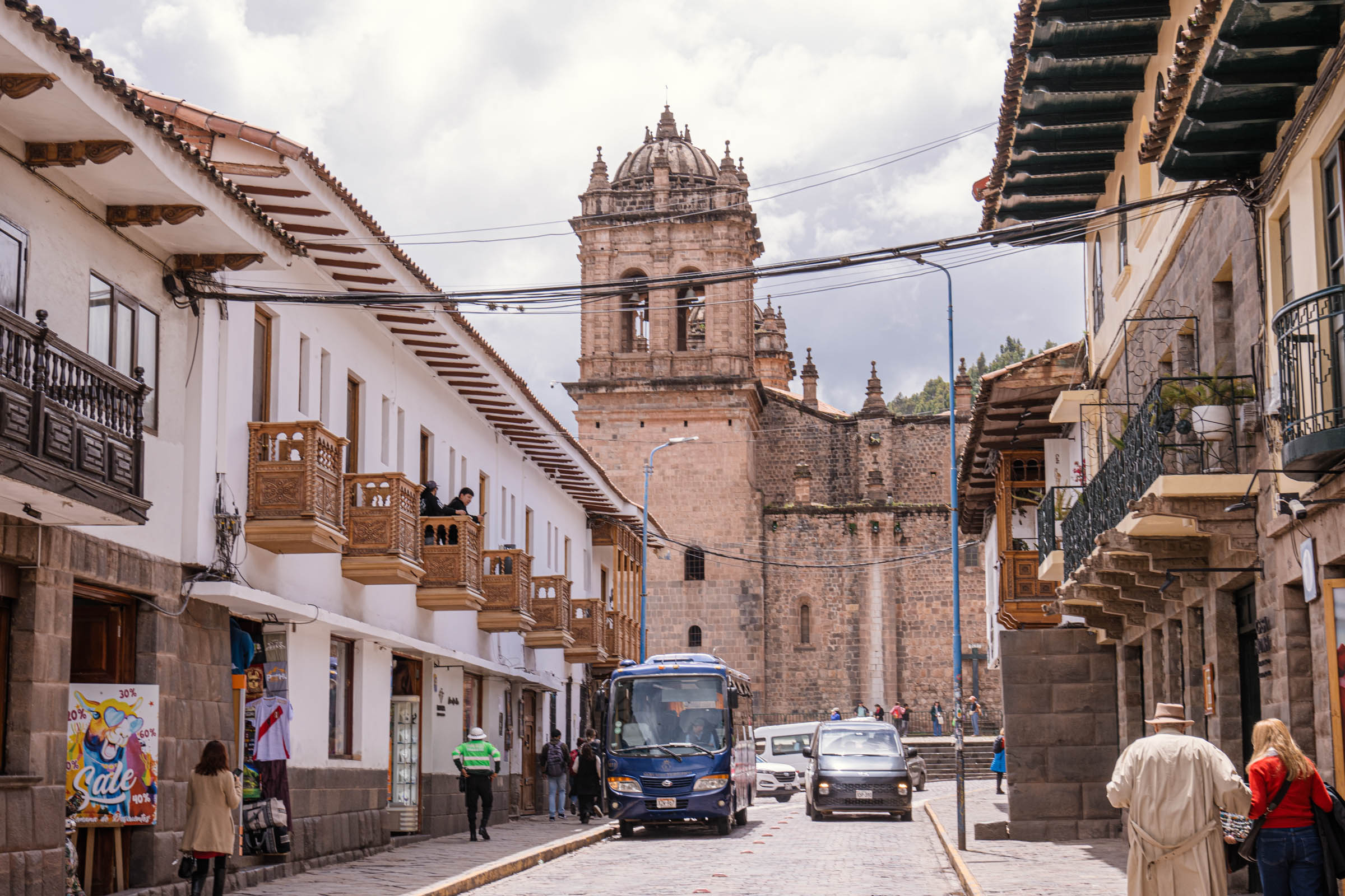 Ulica u Kusku sa turističkim autobusom i lokalnim stanovnicima, sa pogledom na zvonik crkve San Francisco u daljini, svakodnevni život peruvijanskog grada.