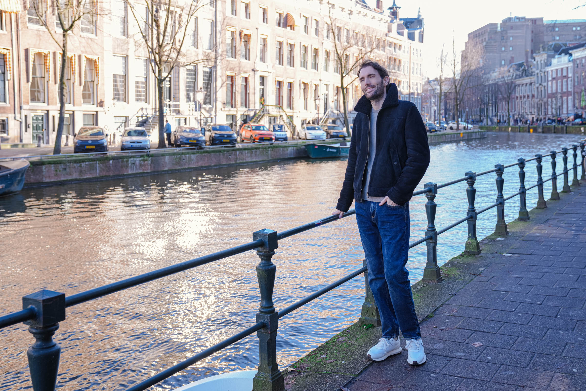 Modni bloger Marko Tadić u pokretu kroz Amsterdam – Façonnable bombarder jakna sa krznom, Alpha Studio kašmir džemper i bele Emporio Armani ASV patike na pozadini holandske arhitekture sa kovanim gvožđem i uljanim lampionima.